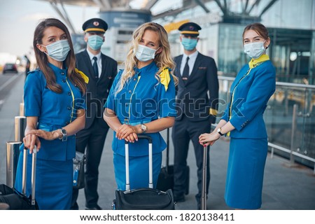 Charming flight attendants and pilots in protective face masks waiting for flight at airport Royalty-Free Stock Photo #1820138411
