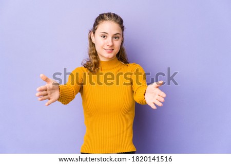 Young caucasian woman on purple background feels confident giving a hug to the camera.