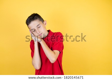 Young beautiful child boy over isolated yellow background sleeping tired dreaming and posing with hands together while smiling with closed eyes.