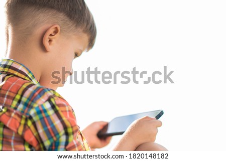 The kid looks into the mobile while sitting in the summer on the street. Small child with a phone in his hands.