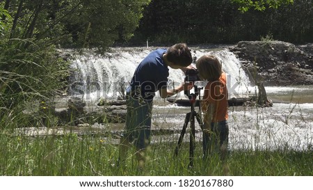 Two children learn to use photo camera, brother catch waterfall landscape 