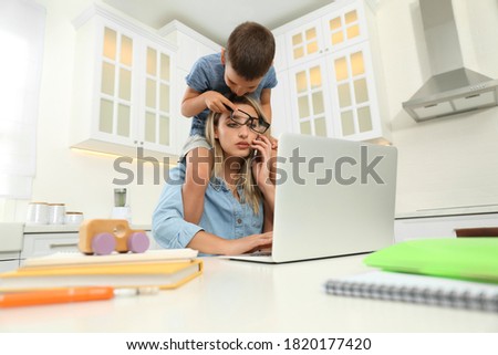 Little boy bothering mother at work in kitchen. Home office concept Royalty-Free Stock Photo #1820177420