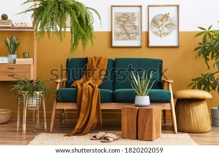 Stylish scandinavian interior of living room with design green velvet sofa, gold pouf, wooden furniture, plants, carpet, cube and mock up poster frames. Template. 