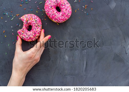 Hand holding donut with icing and sprinkles. Flat lay, top view