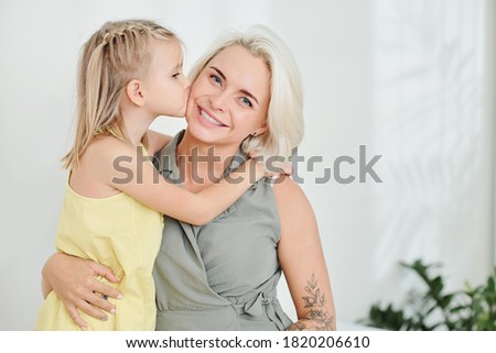 Cute little girl hugging and kissing her smiling mother on cheek