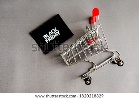 Shopping cart, and a black square that says black Friday on a gray background. The topic of sales.