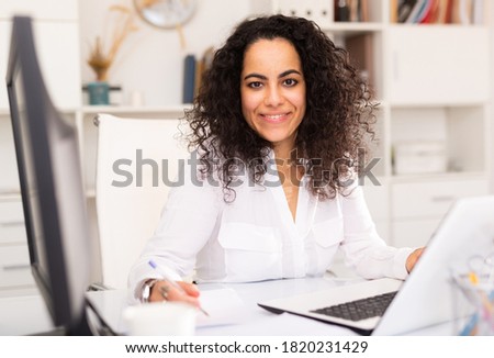 Portrait of young female business employee writing and working with laptop at office