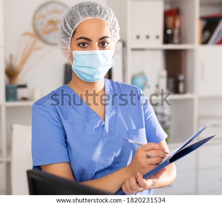 Woman in protective mask is standing with documents in clinic