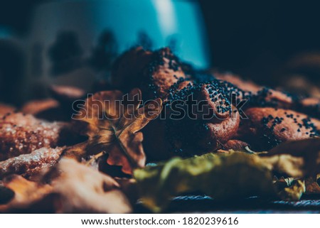 Bun with poppy seeds on an autumn still life with dry oak leaves, warm picture