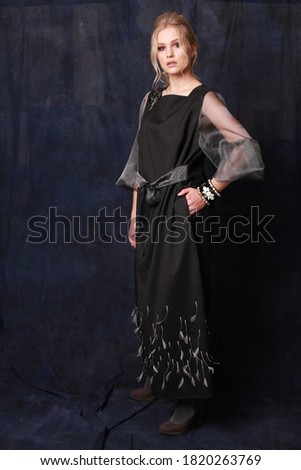 Full length Portrait of a young modern woman dressed with style and taste, posing on a blue fabric background in studio. Model wearing luxury evening dress and outstanding accessories. Catalog shoot 