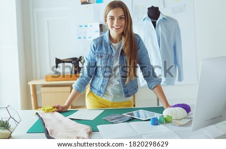 Beautiful fashion designer standing near desk in studio