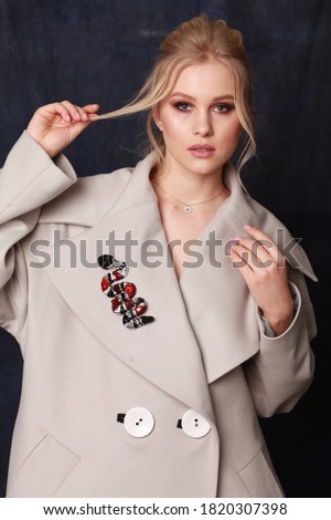 Beautiful, confident and successful woman with make up is posing in stylish coat with bright exclusive accessories (studio shoot of catalogue of fashionable clothes, model demonstrates collection)

