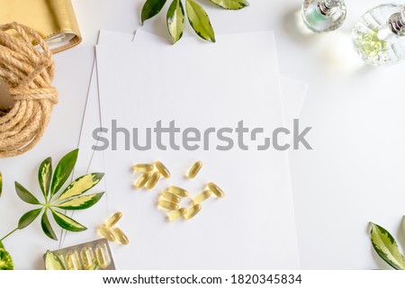 Top view Vitamin Omega-3 capsules on a white background are randomly scattered with place for text . Fish oil blister isolated. Leaves of a shefler plant. Nature positive. Flat lay