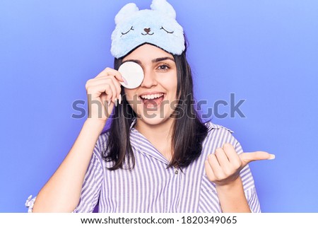 Young beautiful girl wearing funny sleep mask using makeup remover cotton pointing thumb up to the side smiling happy with open mouth  Royalty-Free Stock Photo #1820349065