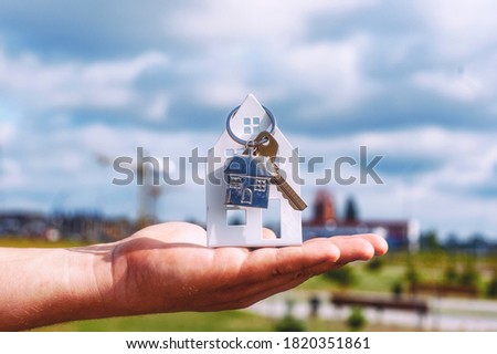 Guy holds the house keys in his hands against the background of clouds. Concept on the topic of buying a new home