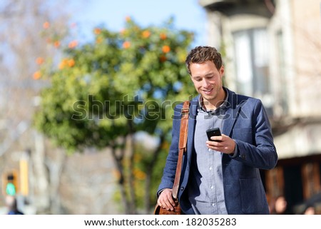 Young urban professional man using smart phone. Businessman holding mobile smartphone using app texting sms message wearing jacket on Passeig de Gracia, Barcelona, Catalonia, Spain. Royalty-Free Stock Photo #182035283