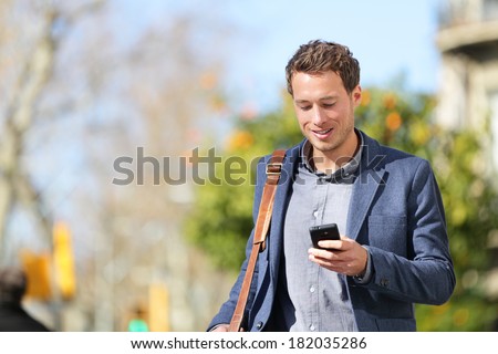 Young urban businessman professional on smartphone walking in street using app texting sms message on smartphone wearing jacket on Passeig de Gracia, Barcelona, Catalonia, Spain. Royalty-Free Stock Photo #182035286