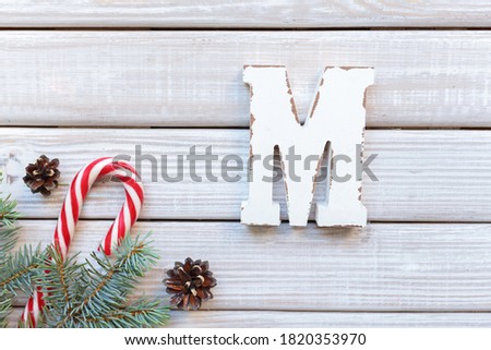 Wooden letter M on white wooden background decorated with spruce branches, pine cones and New Year's lollipop.
Christmas, winter, new year concept. Flat lay, top view