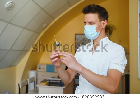male doctor holds syringe while standing in the patient room