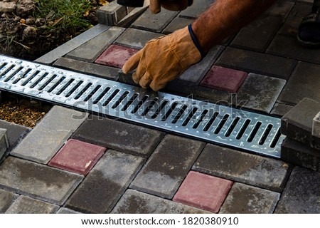 Professional bricklayers install new tiles or slabs for the roadway, sidewalks or patio on a foundation of lined sand. Laying gray concrete paving slabs in the courtyard of the house.