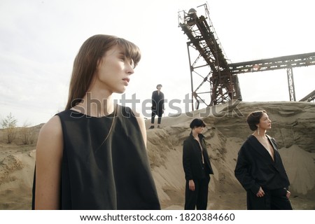 Group of four young beautiful models in desert. Black clothes, high fashion looks, conceptual hairstyle . Metal constructions. Sand. Melancholy mood. Minimalism and japanese design. Good for print