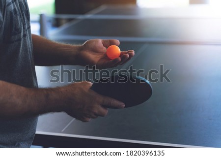 A young man is playing ping pong. He holds a ball and a racket in his hands