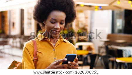 Close up of happy beautiful African American woman texting on smartphone on street.
