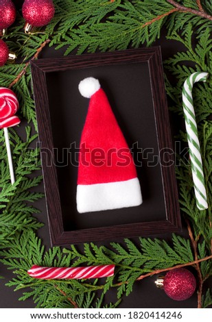 Santa hat in the wooden picture frame, thuja branches, lollipops and baubles around. Christmas background
