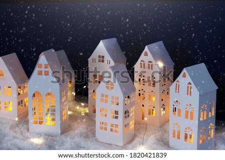 Snowfall in winter village made of paper. Paper winter night landscape. Christmas greeting card.