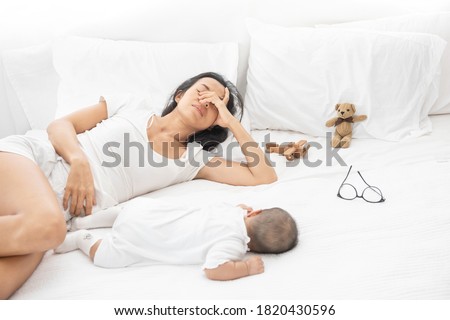 Tired Exhausted Mother Sleeping Sleep With Baby On White Bed. Overwhelmed new asian mom feeling sleep deprived and fatigued with infant at bedroom.