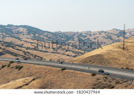 Freeway road with cars crossing the the San Luis Reservoir valleys during dry and hot season, San Luis Creek in the eastern slopes of the Diablo Range of Merced County, California. USA Royalty-Free Stock Photo #1820437964