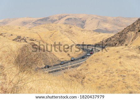 Freeway road with cars crossing the the San Luis Reservoir valleys during dry and hot season, San Luis Creek in the eastern slopes of the Diablo Range of Merced County, California. USA Royalty-Free Stock Photo #1820437979