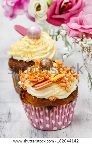 Beautiful cupcakes decorated with yellow and orange sprinkles. Bouquets of pink flowers in the background