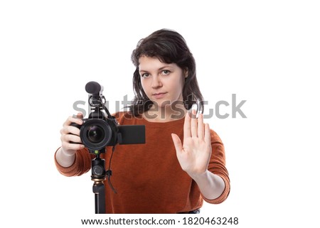Young female with a camera and mic as a filmmaker or online content creator doing a stop gesture.  She looks like a film student or freelancer.  