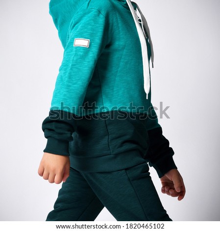 Close up side view of little child hands in sports suit on gray background. Details of clothes for boys, green sports suit for a school student. Children fashion concept.