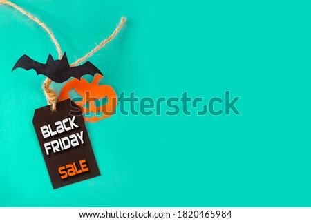 Black Friday and Halloween concept. Black Friday sale tag with bat and jack pumpkin on turquoise with copy space for text or ad