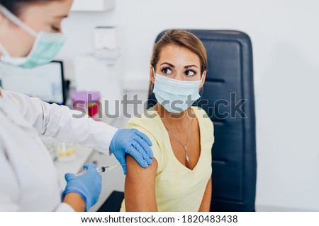 Female doctor or nurse giving shot or vaccine to a patient's shoulder. Vaccination and prevention against flu or virus pandemic.  Royalty-Free Stock Photo #1820483438