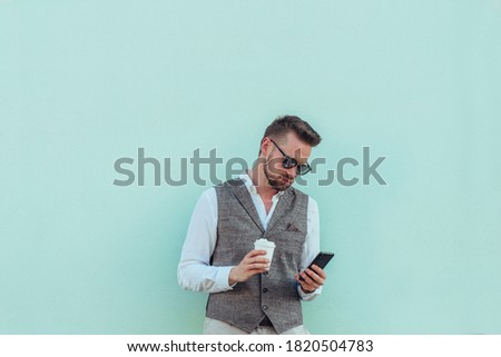 Shot of a well-dressed businessman using a smartphone and drinking coffee in front of a mint colored wall