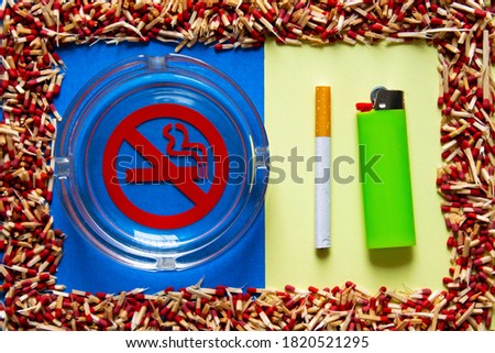 no smoking sign in a glass ashtray with a green lighter and a cigarette next to, in a frame of broken matchsticks, on blue and yellow background