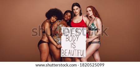Diverse group of women with a signboard of every body is beautiful against brown background. Different size females in bikinis with a placard. Royalty-Free Stock Photo #1820525099
