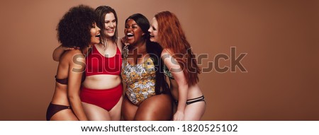 Group of different size females in bikinis laughing together. Multi-ethnic women in swimwear having fun together in studio.