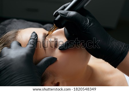 Closeup shot of a woman in black gloves making permanent brow makeup to a young woman in beauty salon Royalty-Free Stock Photo #1820548349