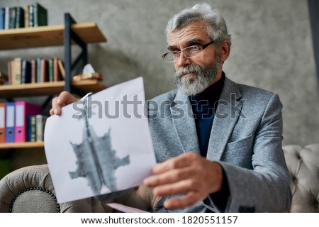 Mature psychologist holding picture with ink stain, Rorschach Inkblot during therapy session. Soldier suffering from depression, psychological trauma. PTSD concept. Focus on picture
