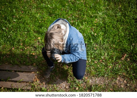 The photographer takes pictures of the grass. The girl learns to photograph. Teenager with a camera in the street. Photography lesson.