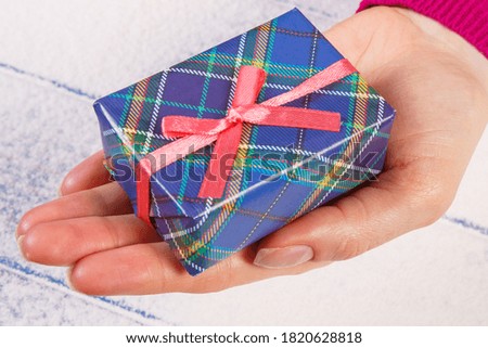 Hand of woman with wrapped colorful gift for Christmas, Valentine, birthday or other celebration on snow background