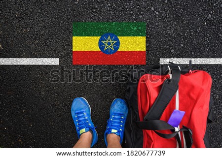 a man with a shoes and travel bag is standing on asphalt next to flag of Ethiopia and border 