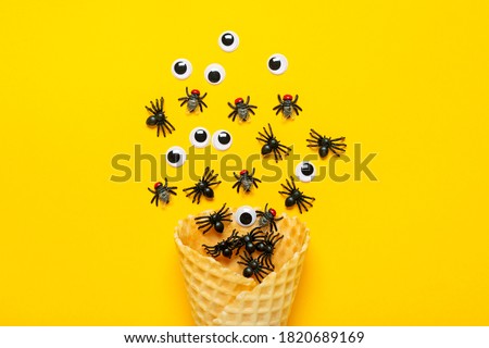 black spiders and flies, 
googly eyes crawl out of ice cream cone on yellow background Top view Flat lay Happy Halloween creative concept Holiday card 