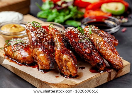American cuisine. Fried chicken wings with tomato sauce and sesame seeds. Serving food in a restaurant on a wooden board. Royalty-Free Stock Photo #1820698616