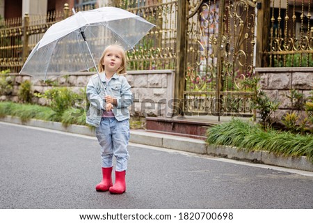 happy child girl with an umbrella and pink rubber boots on an autumn walk. Fall outdoor activity by rainy weather