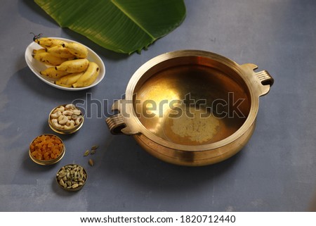 Brass vessel,south indian traditional metal vessel named urule ,which is arranged to make payasam or kheer using cashewnut,kismiss  and cardamom to garnish with grey background,selective focus Royalty-Free Stock Photo #1820712440
